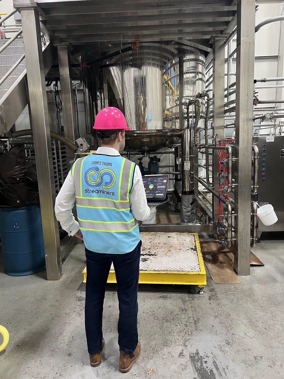 James Thorn on a factory floor, in a hard hat and hi-vis vest, at a process line